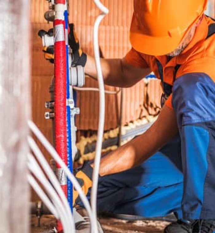 Caucasian Plumber Wearing Orange Hard Hat Installing Bathroom Water Supply Inside Newly Developed Concrete Blocks Building. Construction Site Theme.